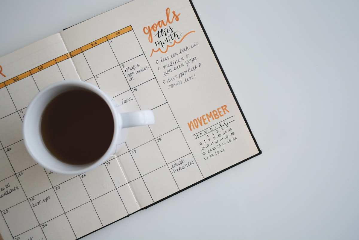 Caderno de planejamento aberto com metas do mês, ao lado de uma xícara de café.