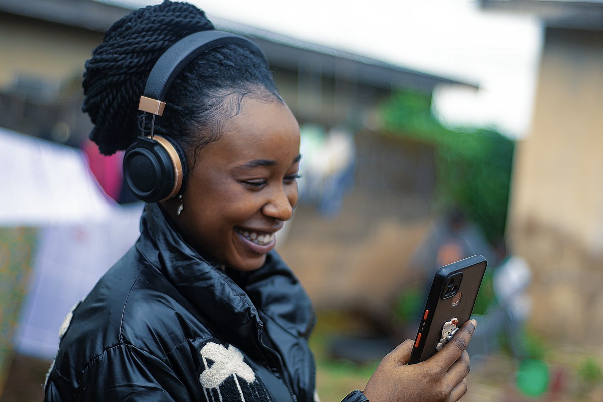 Mulher sorrindo, de fones de ouvido, olhando para o celular.